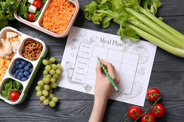 Someone-writing-nutritional-meal-plan-surrounded-by-healthy-food