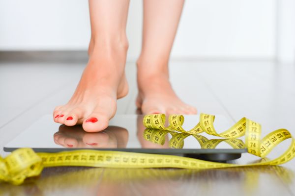 person stepping on scale, weight loss management